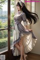 A woman in a dress and hat standing by a window.